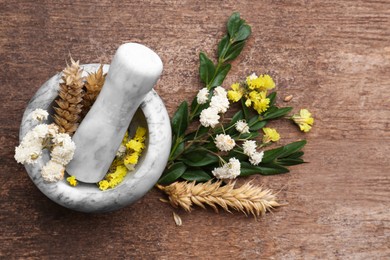 Mortar with pestle, dry flowers and ears of wheat on wooden table, flat lay