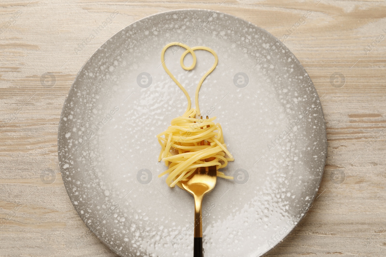 Photo of Heart made with spaghetti and fork on light wooden table, top view