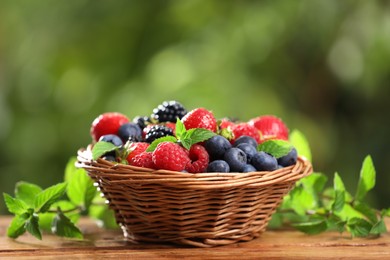 Wicker bowl with different fresh ripe berries and mint on wooden table outdoors