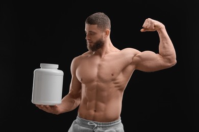 Young man with muscular body holding jar of protein powder on black background