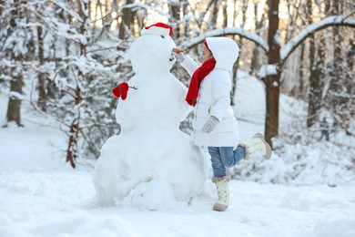 Photo of Cute little girl making snowman in winter park