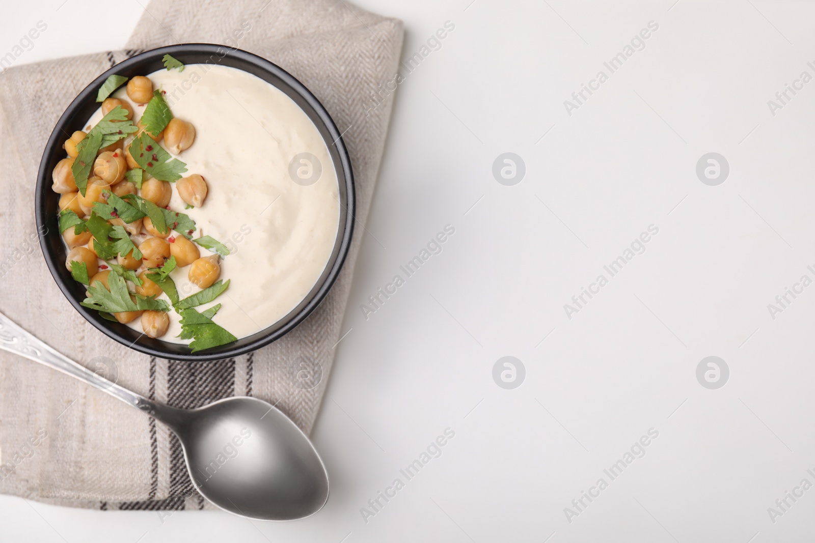 Photo of Tasty chickpea soup in bowl, spoon and napkin on white table, top view. Space for text