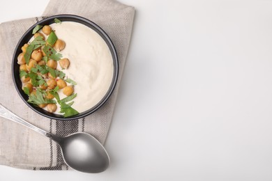Tasty chickpea soup in bowl, spoon and napkin on white table, top view. Space for text