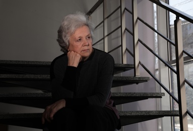 Portrait of poor mature woman sitting on stairs