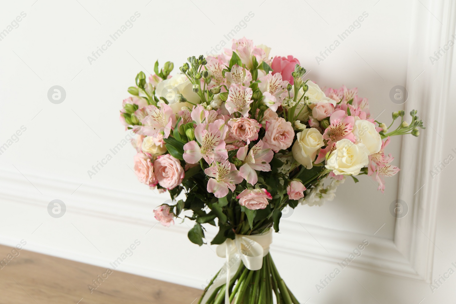Photo of Beautiful bouquet of fresh flowers on wooden table near white wall