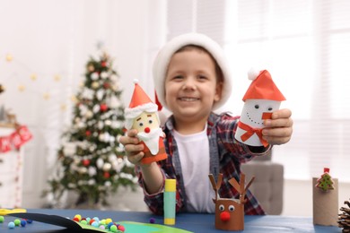Photo of Cute little child with beautiful Christmas crafts at table in decorated room