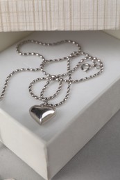 Photo of Metal chain with pendant in box on light table, closeup. Luxury jewelry