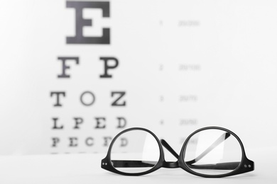 Photo of Glasses with corrective lenses on table against eye chart