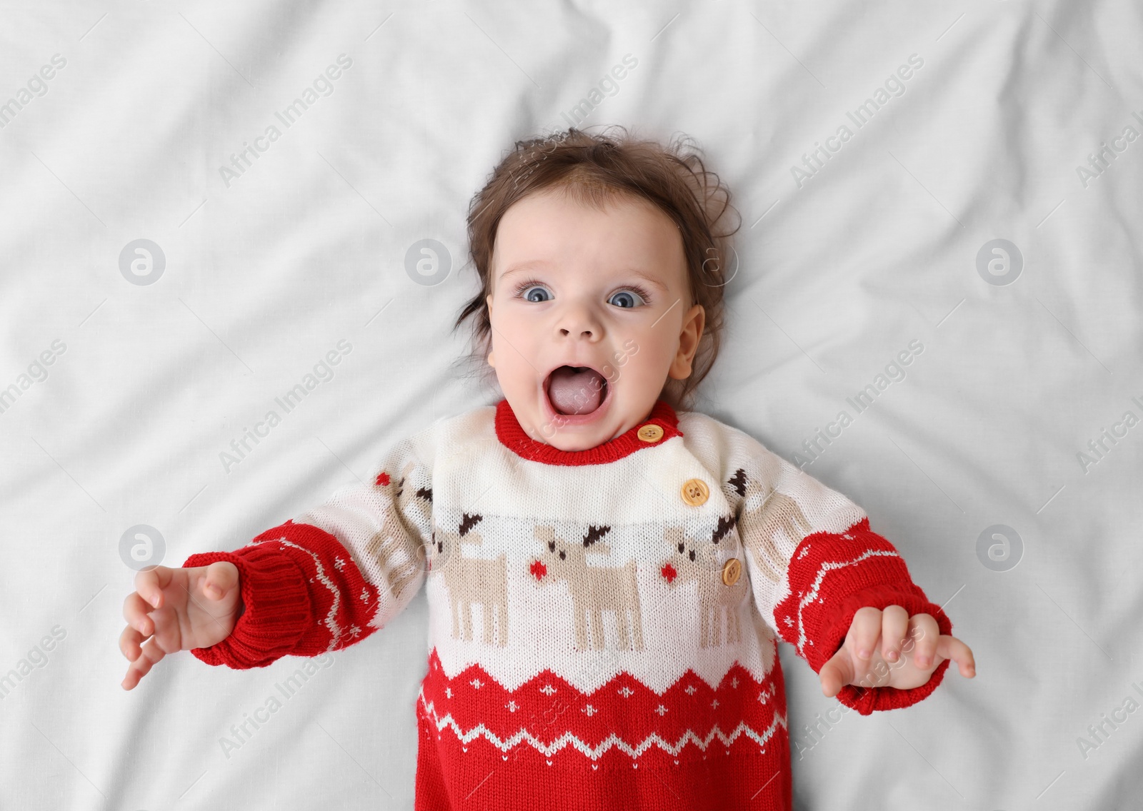 Photo of Cute little baby in Christmas sweater on soft bed, top view