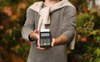 Photo of Man holding payment terminal in floral shop, closeup