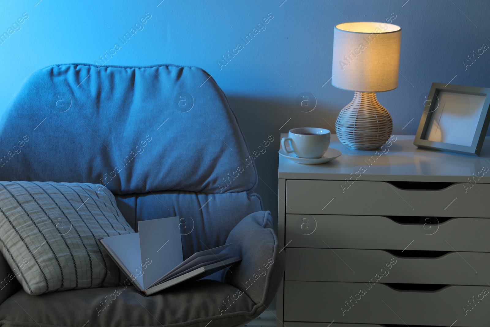 Photo of Comfortable armchair and white chest of drawers in room at night
