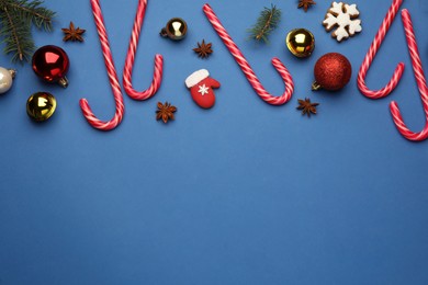 Flat lay composition with sweet candy canes and Christmas decor on blue background, space for text