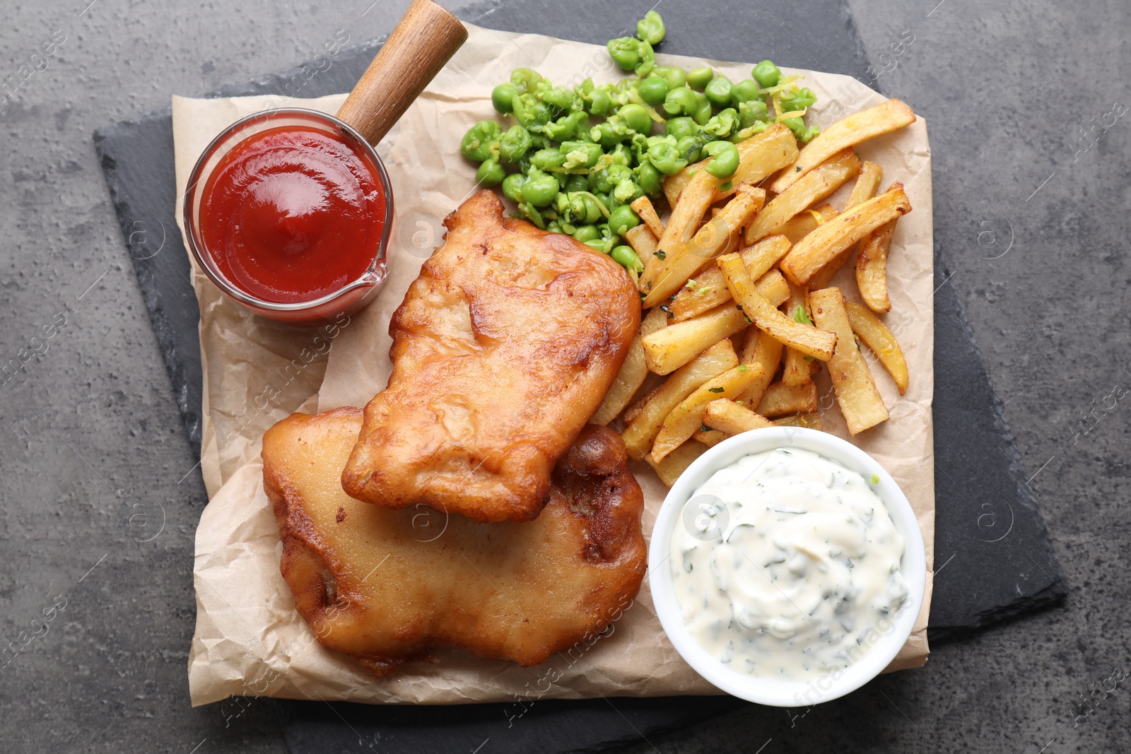 Photo of Tasty fish, chips, sauces and peas on grey table, top view