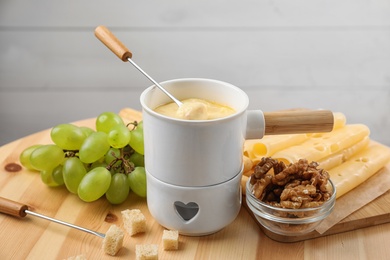 Pot of tasty cheese fondue and fork with bread on wooden table