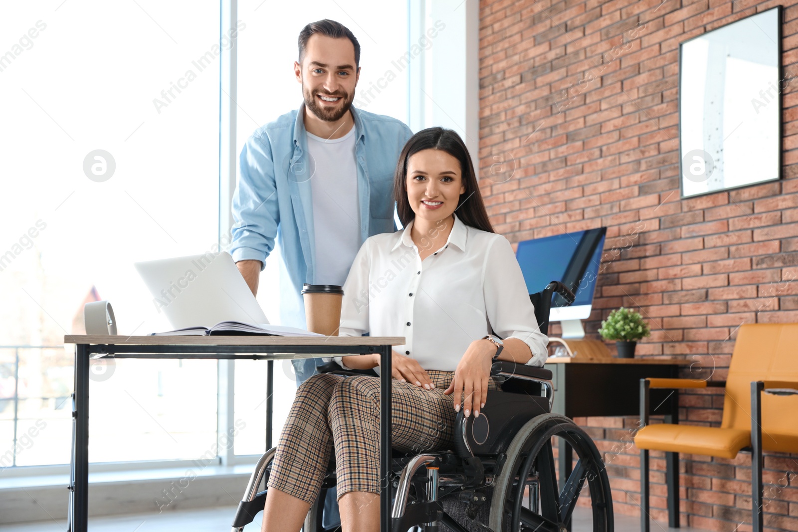 Photo of Young woman in wheelchair with colleague at workplace