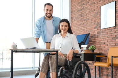 Young woman in wheelchair with colleague at workplace