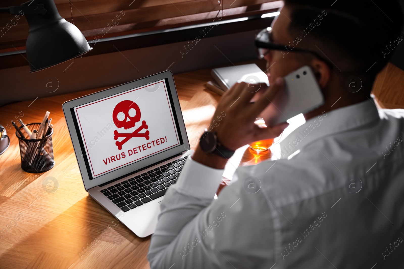 Photo of Man in front of laptop with warning about virus attack at workplace