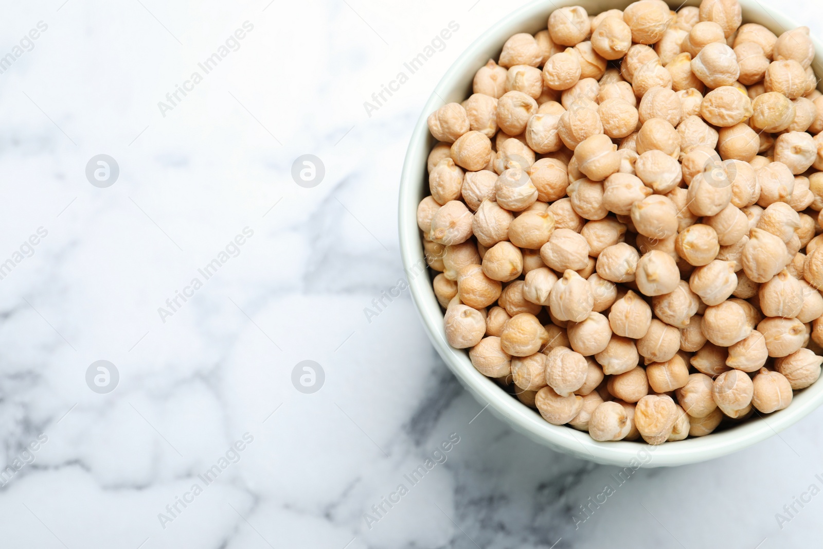 Photo of Chickpeas in bowl on white marble table, top view. Space for text