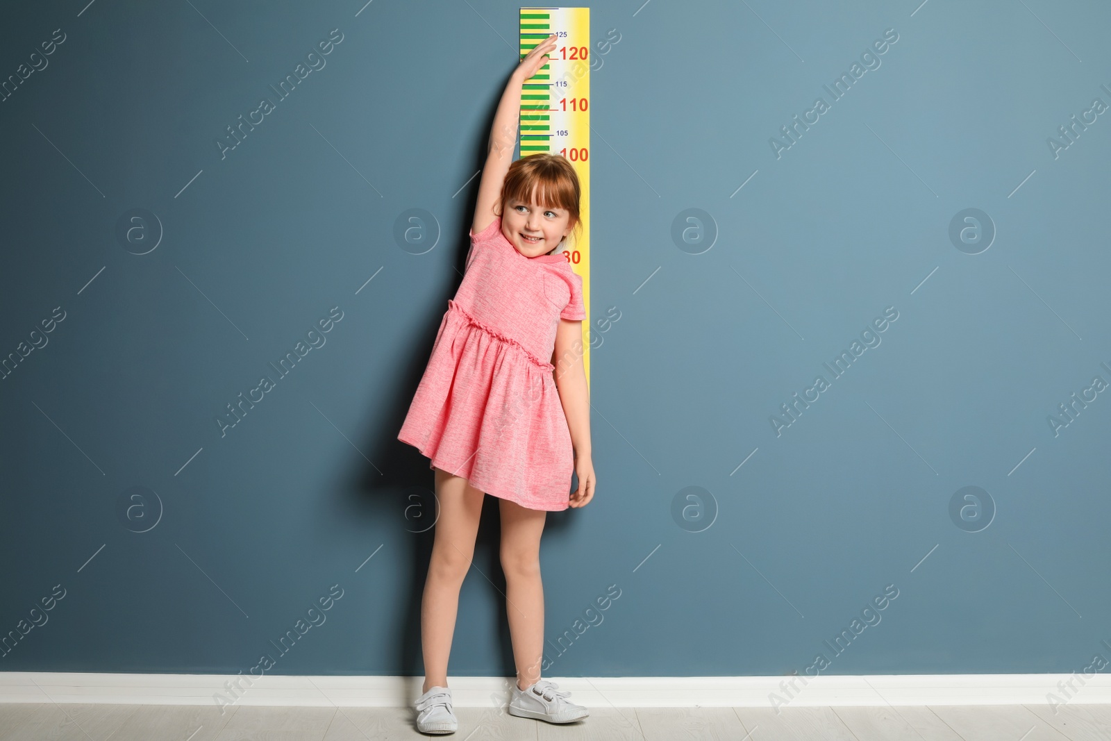 Photo of Little girl measuring her height near color wall