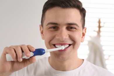 Photo of Man brushing his teeth with electric toothbrush indoors