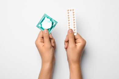 Photo of Woman holding condom and birth control pills on white background, top view. Safe sex