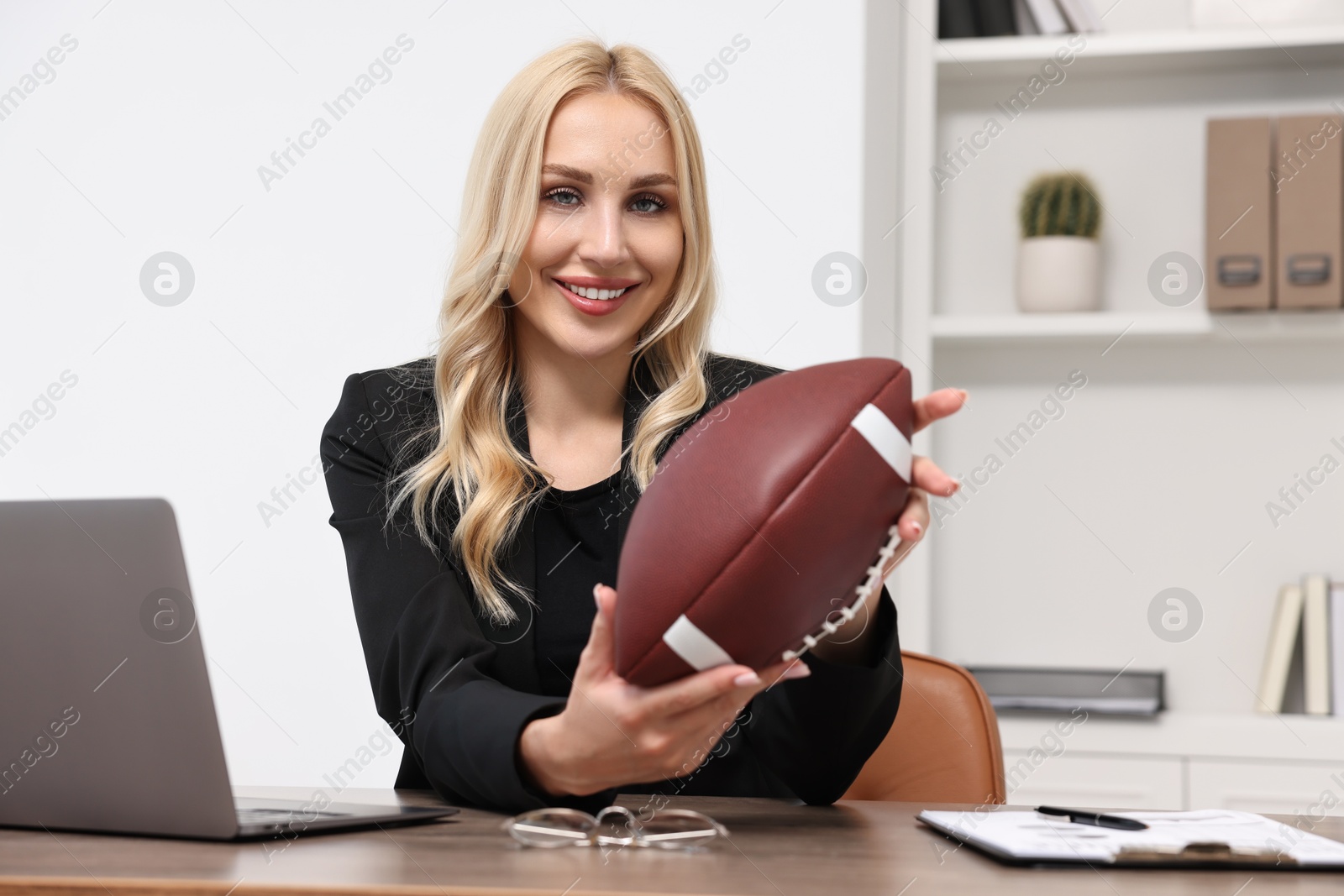 Photo of Happy woman with american football ball at table in office