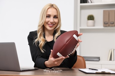 Photo of Happy woman with american football ball at table in office