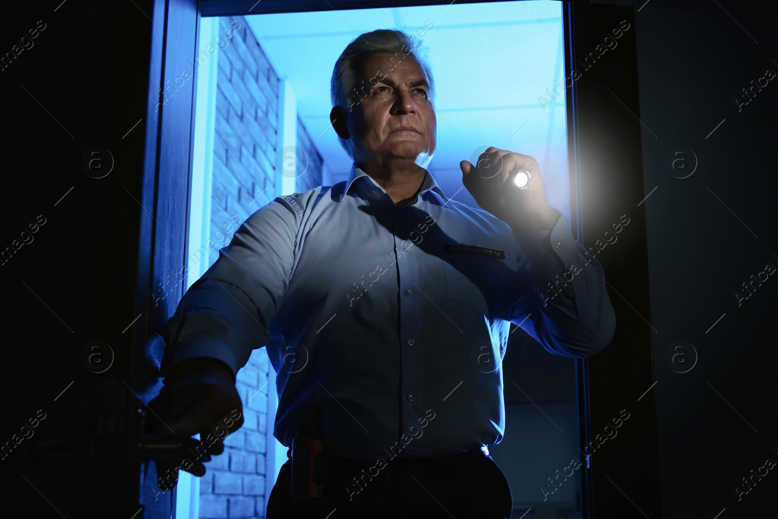 Photo of Professional security guard with flashlight checking dark room