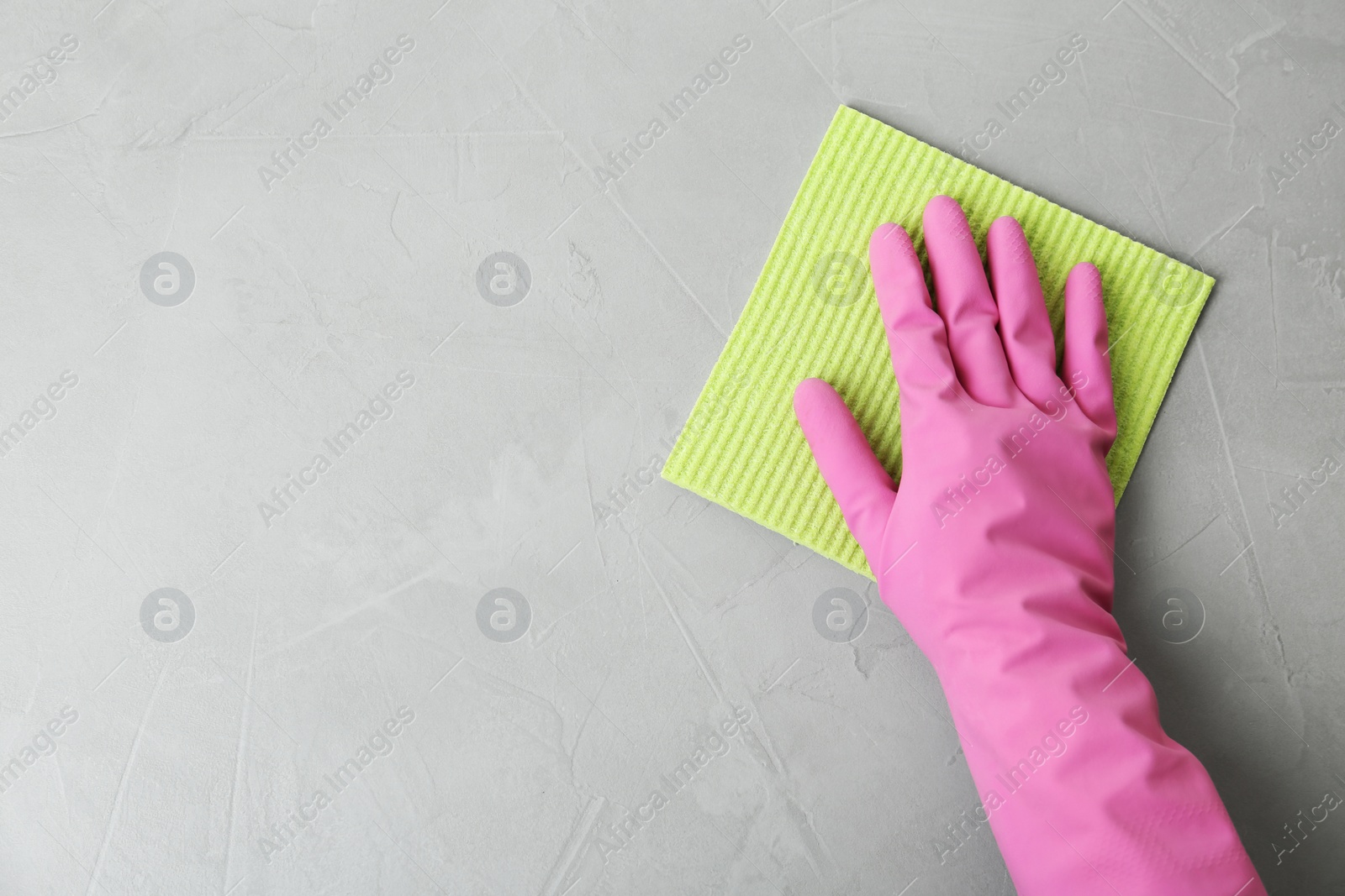 Photo of Woman in gloves wiping grey table with rag, top view. Space for text