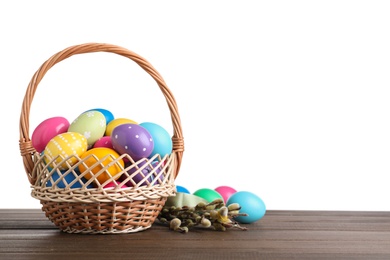 Colorful Easter eggs in wicker basket and willow branches on wooden table against white background. Space for text