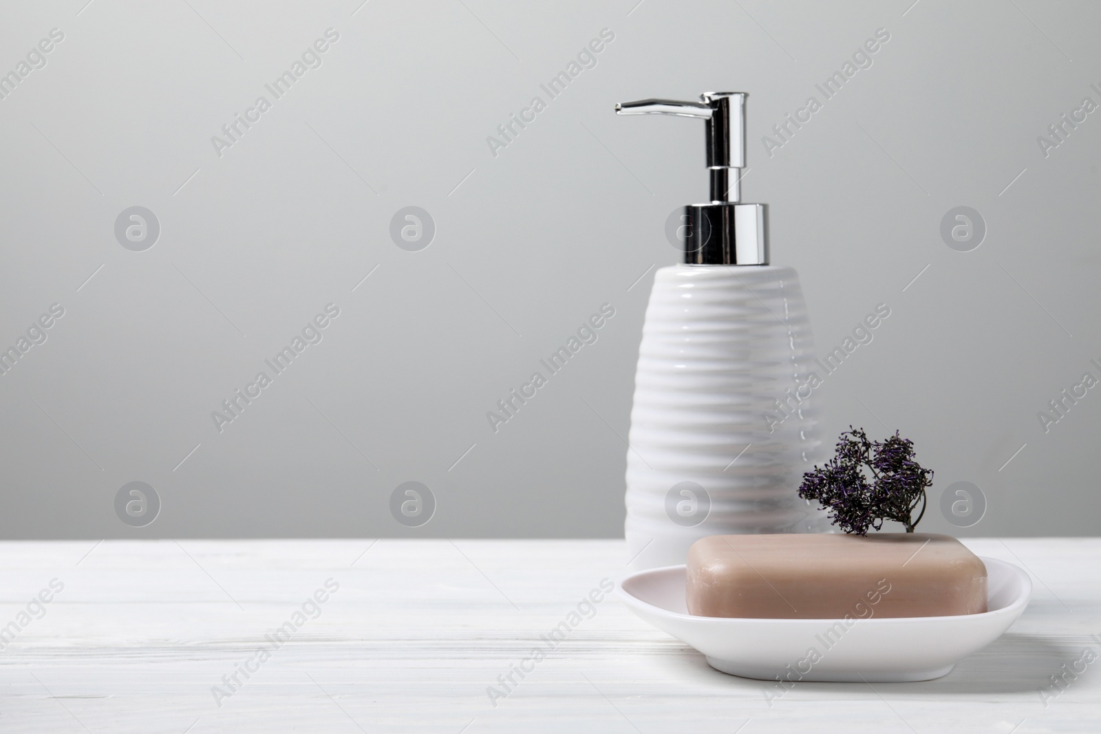 Photo of Soap bar and bottle dispenser on wooden table against white background, space for text