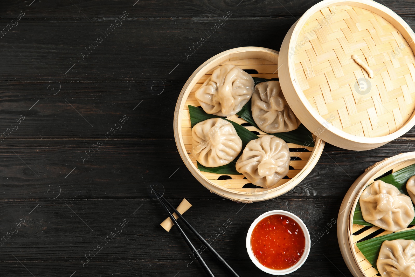 Photo of Bamboo steamers with tasty baozi dumplings, chopsticks and bowl of sauce on wooden background, top view. Space for text