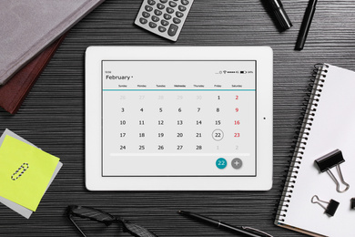 Photo of Flat lay composition of tablet with calendar app on black wooden table