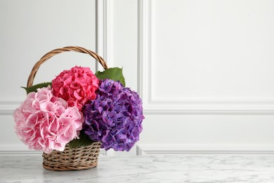 Photo of Bouquet with beautiful hortensia flowers in wicker basket on white marble table. Space for text