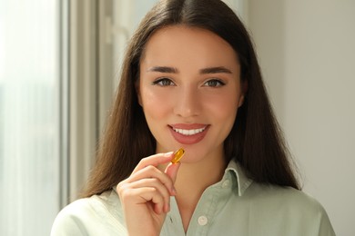 Photo of Young woman taking dietary supplement pill indoors