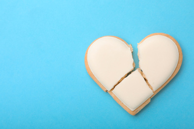 Photo of Broken heart shaped cookie on light blue background, top view with space for text. Relationship problems concept