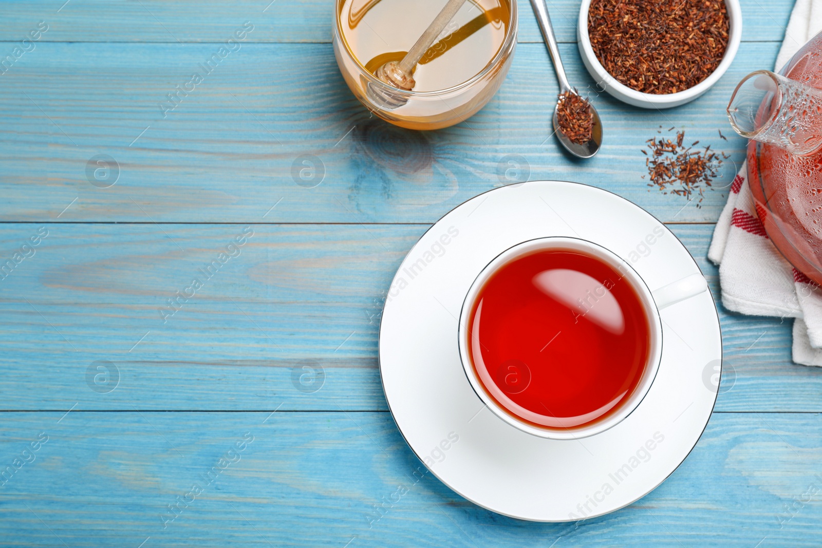 Photo of Freshly brewed rooibos tea and dry leaves on light blue wooden table, flat lay. Space for text