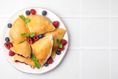 Plate of delicious samosas, berries and mint leaves on white tiled table, top view. Space for text