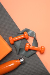 Photo of Dumbbells, thermo bottle, fitness elastic band, yoga block and mat on coral background, flat lay