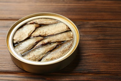 Photo of Open tin can of sprats on wooden table, closeup. Space for text