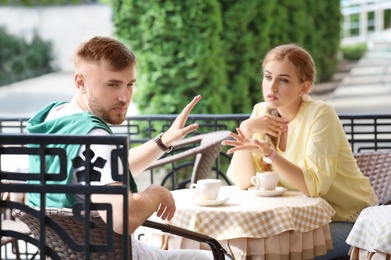 Photo of Young couple arguing while sitting in cafe, outdoors. Problems in relationship