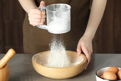 Woman sieving flour into bowl at grey table, closeup