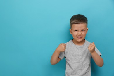 Photo of Angry little boy on light blue background, space for text. Aggressive behavior
