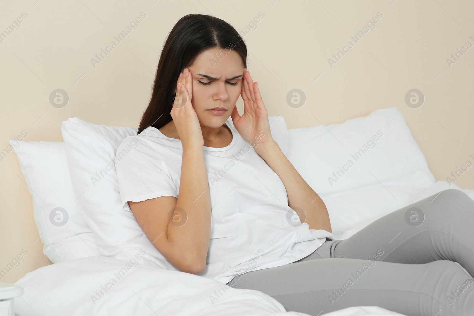 Photo of Young woman suffering from headache on bed indoors. Hormonal disorders