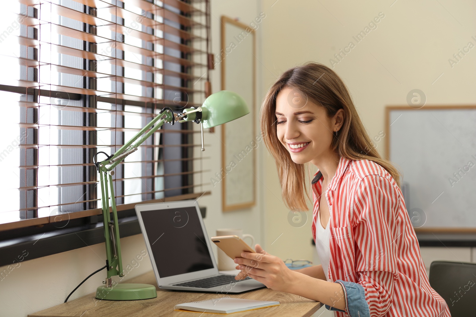 Image of Young woman using phone and laptop at home