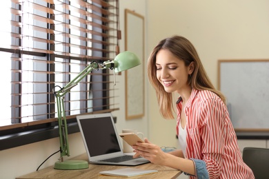 Image of Young woman using phone and laptop at home