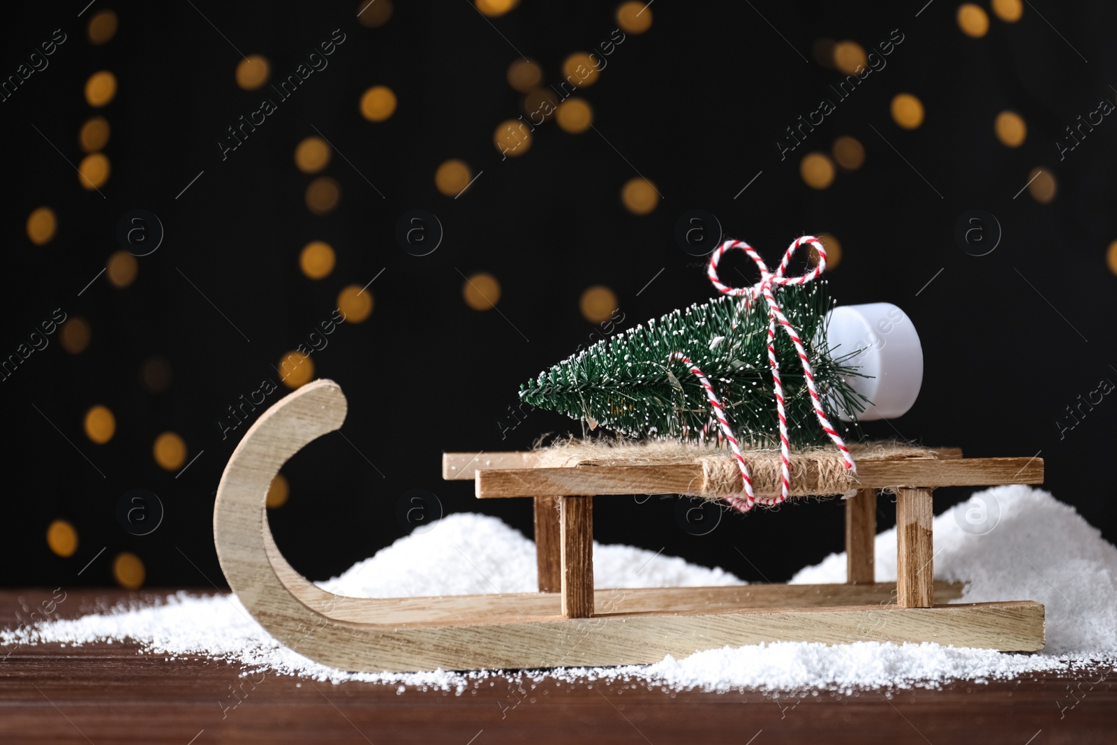 Photo of Sleigh with decorative Christmas tree on wooden table against blurred lights