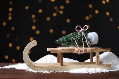 Photo of Sleigh with decorative Christmas tree on wooden table against blurred lights