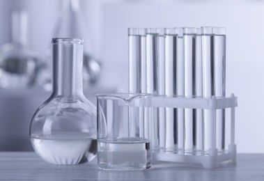 Photo of Different laboratory glassware with transparent liquid on wooden table against blurred background