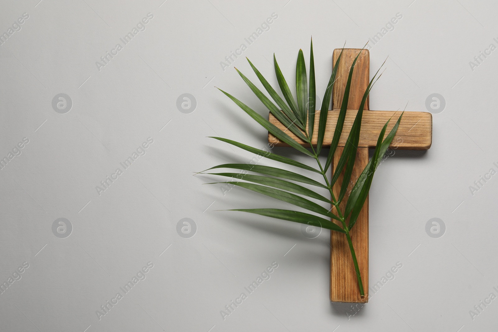 Photo of Wooden cross and palm leaf on light grey background, top view with space for text. Easter attributes